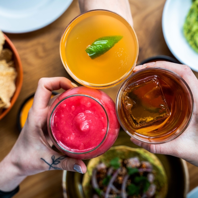 three hands holding drinks at a table