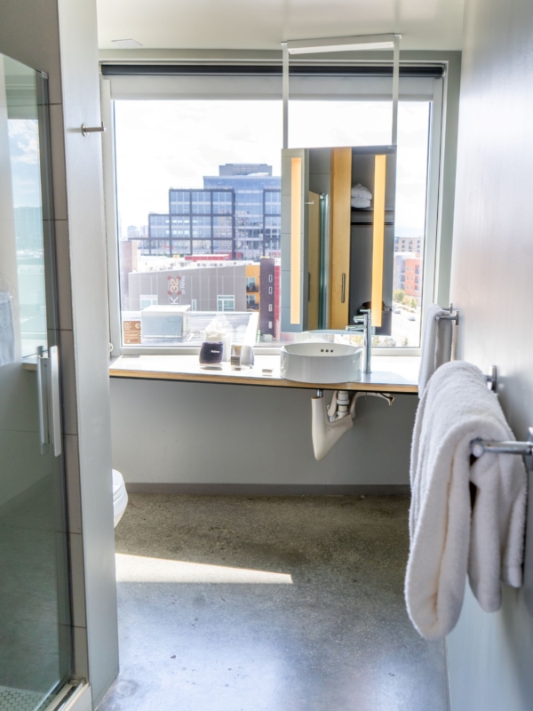 A modern bathroom with a large window, sink, towels, and a shower.